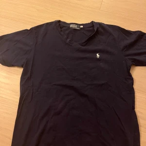 Svart v-ringad t-shirt från Polo - Svart t-shirt från Polo med v-ringning och klassisk broderad logga på bröstet. Tillverkad i 100% bomull och har korta ärmar. Enkel och stilren modell som passar perfekt till jeans eller shorts.