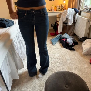 Mörkblå bootcut jeans - Säljer ett par mörkblå jeans med bootcut-modell och låg midja. Jeansen har klassisk femficksdesign och är tillverkade i ett stretchigt denimtyg som sitter snyggt över höfterna och låren innan de blir vidare nertill. Perfekta för dig som gillar en tidlös och trendig look.