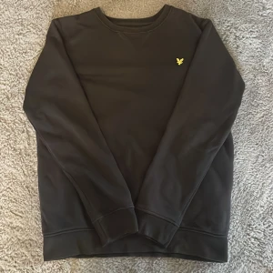 Svart sweatshirt från Lyle & Scott - Svart sweatshirt från Lyle & Scott Junior med klassisk rund hals och broderad gul logga på bröstet. Tröjan är i bra skick endast lite solblekt, passar toppen på någon som är runt 150-155😁