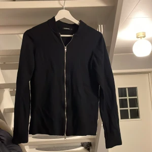 Svart kofta med dragkedja från J.Lindeberg - Mörkblå kofta från J.Lindeberg med hel dragkedja framtill och enkel, stilren design. Långärmad och i mjukt material som passar perfekt till lager-på-lager. Snygg och clean look som funkar till det mesta. Storlek s men passar även xs