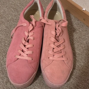 Rosa mockasneakers från Vagabond - Snygga rosa sneakers från Vagabond i mjuk mocka. Skorna har klassisk rund tå, platt sula och snörning framtill. Perfekta för dig som vill ha en stilren och trendig look med en poppig färg. Diskret Vagabond-logga på hälen och stilren design.