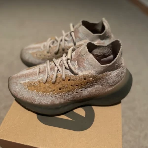 Adidas Yeezy Boost 380 i beige toner - Säljer ett par Adidas Yeezy Boost 380 med stickad ovandel i beige, bruna och grå toner. Skorna har ett unikt mönster, rund tå, snörning och en chunky, mörk sula. Perfekta för dig som gillar streetwear och vill sticka ut med en futuristisk sneaker.