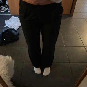 Svarta kostymbyxor med raka ben - Snygga svarta kostymbyxor med raka ben och klassisk passform. Byxorna har låg midja, diskreta fickor fram och stängs med knapp och dragkedja. Perfekta för en clean och stilren look.