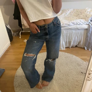  blå slitna jeans - jeans med hög midja och raka ben. Jeansen har slitna detaljer och hål på båda knäna för en cool, avslappnad look. Klassisk femficksmodell i kraftigt denimtyg. Perfekta för dig som gillar vintage vibe.