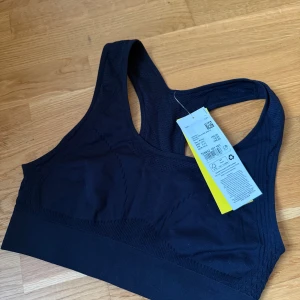 Svart sport-bh från Röhnisch - Svart sport-bh från Röhnisch med bred resår nedtill och brottarrygg. Tillverkad i ett stretchigt och mjukt material som andas, perfekt för träning. Snygg, sömlös design med diskreta mönsterdetaljer och meshpartier för extra ventilation.