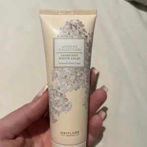 Oriflame Innocent White Lilac handkräm - En parfymdoftande handkräm från Oriflame, Women's Collection Innocent White Lilac. Tuben är ljusbeige med blommigt mönster i vitt och grått. Innehåller 75 ml och har en söt, blommig doft av vit syren. Perfekt att ha i väskan för mjuka händer.