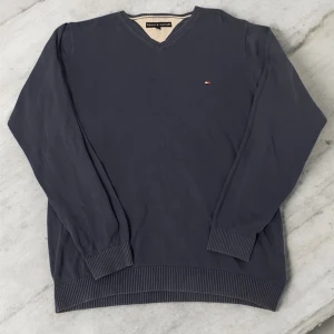 Mörkblå v-ringad tröja Tommy Hilfiger - Klassisk mörkblå v-ringad tröja från Tommy Hilfiger i bomull. Tröjan har ribbade muddar och nederkant samt en liten broderad logga på bröstet. Perfekt för dig som gillar stilrena och tidlösa plagg. Använd ett par få gånger men passar tyvärr inte längre mig. 