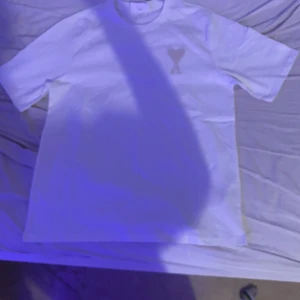 Vit t-vshirt från Ami Alexandre Mattiussi - Vit t-shirt från Ami Alexandre Mattiussi med klassisk passform och korta ärmar. På bröstet finns det ikoniska broderade hjärtloggan i vitt. Tillverkad i mjuk bomull och har rund halsringning. Perfekt för en clean och stilren look.