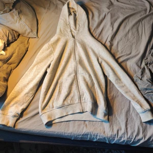 Ljusgrå hoodie med dragkedja från lager 157 - Ljusgrå hoodie från lager 157 med hel dragkedja framtill och två fickor. Tröjan har huva med snörning och är tillverkad i mjukt material, perfekt för chill dagar. Klassisk passform och ribbade muddar vid ärmslut och nederkant.