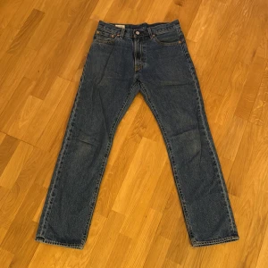 Levi's 551 blå jeans straight fit - Klassiska Levi's 551 jeans i blå denim med raka ben och normal passform. Byxorna har fem fickor, orange kontrastsömmar. Perfekta för dig som gillar tidlös stil och vill ha ett par jeans som funkar till allt. Ett par byxor som passar till allt. Säljer då dom inte passar mig längre.