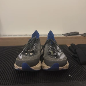 Adidas Adizero Boston 12 löparskor - Säljer ett par Adidas Adizero Boston 12 löparskor i grått och blått med vita detaljer. Skorna har mesh-ovandel för bra andningsförmåga, svart snörning och en tjock, dämpad sula med Lightstrike Pro-teknologi. Perfekta för dig som gillar att springa snabbt och bekvämt. ( äkta morsan jobbar där)