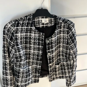 Svartvit rutig jacka  - Snygg svartvit kavaj i rutigt bouclétyg med rund halsringning och dekorativa knappar framtill. Jackan har två fickor och är fodrad, perfekt för att lyfta din outfit med en klassisk touch. Aldrig använd 