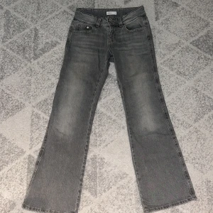 Grå jeans från Gina tricot, stl 34 - Snygga grå jeans från Gina tricot i rak modell med klassiska fem fickor och dubbla knappar i midjan. Jeansen har en tvättad look och raka ben, perfekt för en avslappnad stil. Materialet är mjukt denim och färgen är en cool, lite sliten grå.
