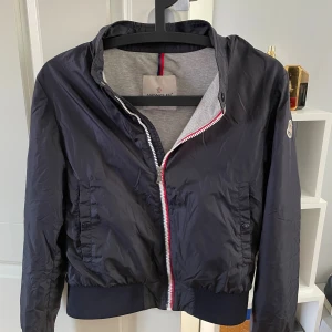 Mörkblå vindjacka från Moncler - Snygg mörkblå vindjacka från Moncler. Jackan är i storlek 164 men sitter lite mer som 158 skulle jag säga, jackan är i skitbra skick och är knappt använd! Hör av dig direkt vid frågor eller funderingar!😃🙌