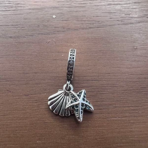 Berlock till Pandora armband  - Hängande berlock med snäcka och sjöstjärna med blåa stenar i silver till Pandora armband. Så gott som nytt. Använt färre än 10 gånger. (Armband ingår ej i priset)