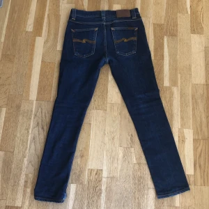 Mörkblå slim fit jeans från Nudie - Snygga mörkblå jeans från Nudie med klassisk femficksdesign och kontrastsömmar. Modellen är slim fit med smala ben och Nudies ikoniska logga på bakfickorna. W29 L30 men passar bättre på W28 L30