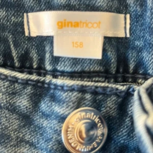Blå bootcut jeans från Gina Tricot - Snygga blå jeans från Gina Tricot i storlek 158. Modellen har bootcut-ben och klassisk femficksdesign med broderade bakfickor. Jeansen är tillverkade i denim och har en cool tvättad look med knäppning framtill.