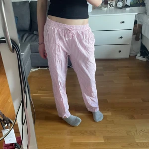 Rosa randiga linnebyxor från 157 XS - Lätta och luftiga linnebyxor från 157 i storlek XS. Byxorna är rosa med vita ränder, har resår och snörning i midjan för skön passform. Perfekta för varma dagar när du vill ha något bekvämt och stilrent.