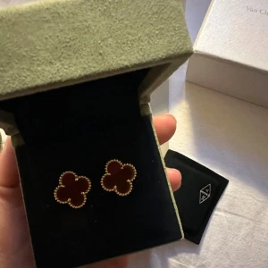 Van Cleef & Arpels Alhambra örhängen - Exklusiva Alhambra örhängen från Van Cleef & Arpels i fyrklöverform. De har en djup röd mitt och är omgivna av detaljerad guldfärgad kant. Ikonisk design som verkligen sticker ut och ger en lyxig känsla till din stil. Kommer med box, kvitto, certifikat.