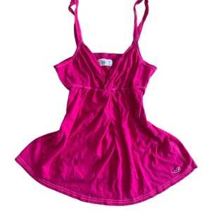 Rosa linnetopp från Hollister - Supersöt rosa linnetopp från Hollister med smala axelband och lätt v-ringad front. Toppen har en twistad detalj vid bysten och är utsvängd nertill. Broderad Hollister-logga nertill. Perfekt för varma dagar och enkel att styla med jeans eller shorts.