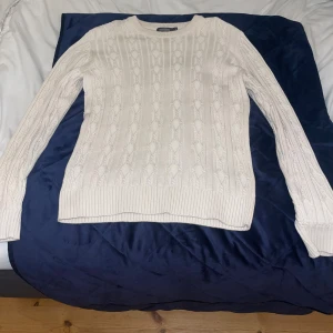 Vit stickad tröja från Dressmann - Säljer en beige stickad tröja från Dressmann i storlek M. Tröjan har ett klassiskt kabelstickat mönster, rund halsringning och långa ärmar. Perfekt för dig som gillar en stilren och tidlös look.
