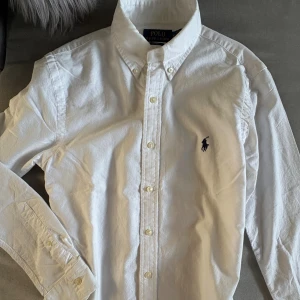 Polo Ralph Lauren Skjorta (XS) - Säljer min brors klassiska vita skjorta från Polo Ralph Lauren i slim fit-modell. Skjortan har lång ärm, knappar framtill och ikoniska broderade loggan på bröstet. Tillverkad i mjuk bomull. S