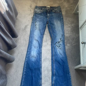 Blå bootcut jeans med slitningar - Snygga blå jeans från Gina tricot  med bootcut passform och slitna detaljer på benen. Jeansen har klassisk femficksdesign, låg midja och är tillverkade i denim med cool tvätt och slitningar för en trendig look. Innerbens längd 77cm Midje mått 31 cm. Priset kan diskuteras skulle inte säga med lågmidja men de är inte jätte högmidjade men lite mer mot de höga hållet 