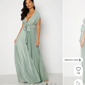 Ljusgrön långklänning från Goddiva - Aldrig använd. Supersnygg ljusgrön långklänning från Goddiva i satinliknande polyester. Klänningen har v-ringning, omlottliv och breda band som kan knytas på flera sätt. Perfekt för dig som vill ha en elegant och flowy look med extra volym i kjolen.