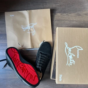 Christian Louboutin svarta sneakers mocka - Svarta sneakers från Christian Louboutin i mocka med klassisk röd sula och snörning. Snygg och stilren design med rund tå och diskreta detaljer. Perfekta för dig som vill sticka ut med exklusiva skor och ikonisk look.