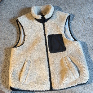 Beige teddyväst från Vero Moda - Mysig beige teddyväst från Vero Moda med hög krage och svarta detaljer.