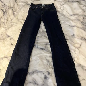 Mörkblå jeansbyxor från 157, XXS - Mörkblå jeansbyxor från 157 i storlek XXS med full längd. Klassisk femficksmodell med snygga bakfickor med lock och silverfärgade knappar. Jeansen har raka ben och normal passform, perfekta till en avslappnad stil.