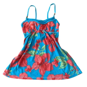 Vintage Blommig blå Topp Hollister - Superfin topp från Hollister i klarblått med stora röda blommor och gröna blad. Toppen har smala axelband med små träpärlor och en söt rynkdetalj under bysten. Mjuk bomull som känns lätt och somrig.