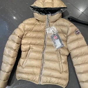 Beige pufferjacka från Colmar - Snygg beige pufferjacka från Colmar med huva och dragkedja framtill. , två fickor med dragkedja och en rund Colmar-logga på ärmen. Perfekt för kyliga dagar och riktigt skön att bära. Inga defekter och är helt som ny, säljer pågrund av att den är för liten för mig