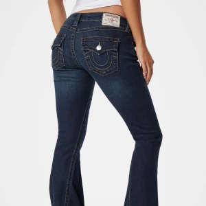 True Religion mörkblå bootcut jeans - Mörkblå jeans från True Religion i modellen Joey med bootcut passform och snygga kontrastsömmar. Klassiska fickor bak med silverfärgade knappar. Jeansen har låg midja och är tillverkade i stretchig denim för en bekväm känsla. Jag har sytt upp dom lite men dom är fortfarande för långa på mig som är 155cm. Sparsamt använd.