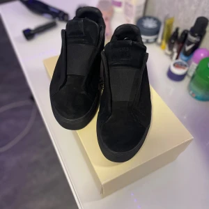 Svarta sneakers från Axel Arigato mocka - Snygga svarta sneakers från Axel Arigato i mocka med minimalistisk design. Skorna har elastiskt band över vristen istället för klassisk snörning och en platt svart sula. Perfekta för dig som gillar stilrena och moderna skor.