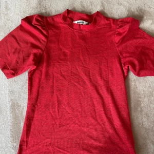 Röd topp med puffärm från Kappahl - Säljer en röd topp från Kappahl i storlek XS. Toppen har korta puffärmar och en lite högre rund halsringning. Materialet är mjukt och stretchigt, perfekt för dig som gillar en enkel men ändå trendig look.