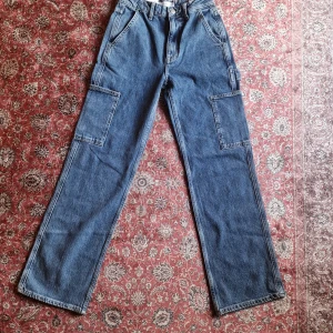 Blå cargo jeans från C XS - Säljer ett par blå cargo jeans från C i storlek XS. Byxorna har raka ben, stora cargofickor på sidorna och klassiska jeansdetaljer. Tillverkade i denim med bälteshällor och knappgylf. Perfekta för en avslappnad och trendig look.Nypris 599kr