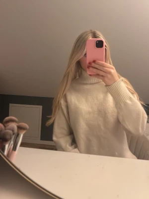 Vit polotröja i stickat material - Mysig vit polotröja med ribbade muddar och hög krage. Tröjan är stickad och har en relaxed, lite oversized passform som är perfekt för kyliga dagar. Enkel att styla med jeans eller kjol för en clean look.