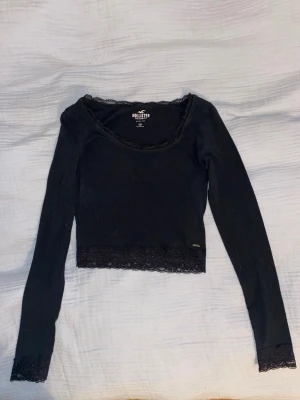 Svart spetsdetaljerad topp Hollister - Säljer en svart långärmad topp från Hollister med fina spetsdetaljer vid halsringning, ärmslut och nederkant. Inte använd av mig. skriv om ni undrar om något 💕