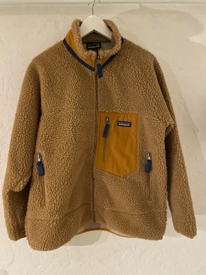 Beige fleecejacka från Patagonia - Säljer en beige fleecejacka från Patagonia med hög krage och dragkedja framtill. Perfekt för kalla dagar och riktigt mysig att bära. Storlek M, nytt skick använd enstaka gånger.
