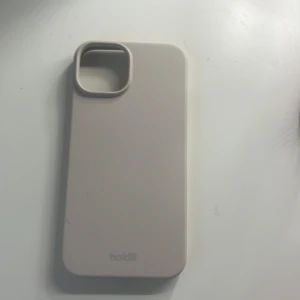 Beige mobilskal från Holdit - Säljer ett stilrent beige mobilskal från Holdit. Skalets design är enkel och slät, med en mjuk känsla och diskret logga längst ner. Passar perfekt för dig som vill ha ett minimalistiskt och snyggt skydd till mobilen. Användt endast 1 gång. iPhone 13 