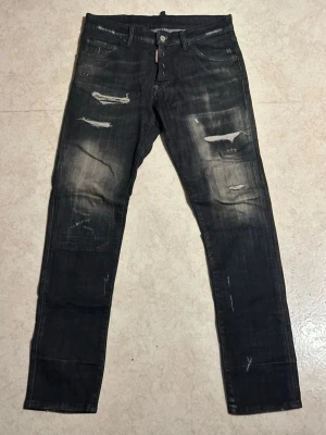 Svarta Dsquared2 jeans med slitningar - Säljer ett par svarta jeans från Dsquared2 med snygga slitningar och distressed detaljer på både fram- och baksida. Jeansen har en rak passform och klassisk femficksdesign. Materialet är robust denim i bomull och de har en cool, lite tvättad look. Tveka inte om du har frågor eller vill sänka priset. Vill bara få sålt på dessa❗️