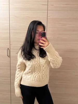 Beige stickad tröja med flätmönster - Supermysig beige stickad tröja med grovt flätmönster och rund hals. Tröjan har lång ärm och en loose fit som ger en chill vibe. Perfekt att slänga på sig när det är kallt ute.