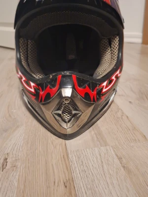 Takachi blå och svart hjälm med flames - Säljer en riktigt cool Takachi hjälm i svart och blått med röda och vita flames på sidorna. Hjälmen har ett sportigt mönster och ventiler framtill. Perfekt för dig som vill sticka ut med en unik look. Lite skrap märken men det stoppar inte hjälmen  