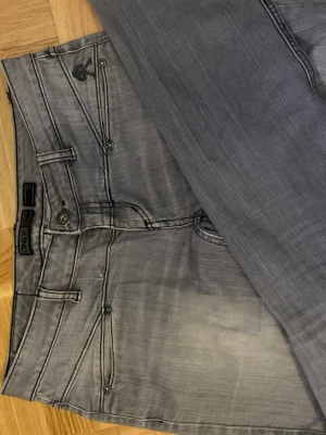 Grå vintage lågmidjade jeans från ONLY - Säljer ett par grå jeans från ONLY Limitless Denim med snygga detaljerade sömmar och unika fickor både fram och bak. Jeansen har normal passform och klassisk knappgylf. Perfekta till en chill vardagslook. Dom är vintage lågmidjade och jeansen liknar LTBs jeans i benen.