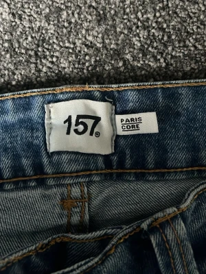 Blå bootcut jeans från 157, XS - Säljer ett par klassiska blå jeans från 157 i modellen Paris Core. Jeansen har bootcut-ben, full längd och dubbla knappar i midjan. Snygga kontrastsömmar och femficksmodell. Perfekta till sneakers eller boots.