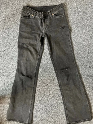 Lågmidjade bootcut jeans - Säljer ett par svarta jeans från Monki med bootcut passform och slitna detaljer på benen. Perfekta för dig som gillar en avslappnad men ändå trendig look.