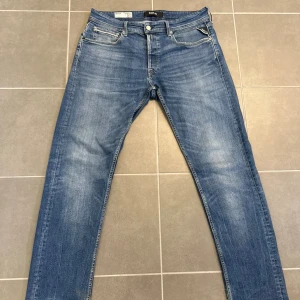 Replay Grover blå jeans, W34 L32 - Säljer ett par Replay Grover jeans i klassisk blå tvätt med snyggt slitna detaljer. Jeansen har fem fickor, raka ben och normal passform. Märkesdetaljer på ficka och bak med läderpatch. Perfekta för dig som gillar stilrena och bekväma jeans.