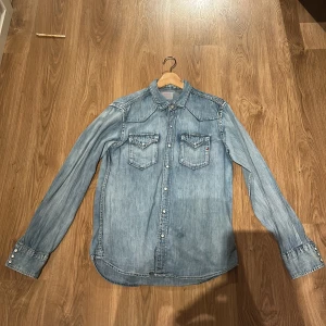 Ljusblå jeansskjorta från Replay - Säljer en klassisk ljusblå jeansskjorta från Replay med tryckknappar och två bröstfickor. Skjortan har lång ärm, snygga detaljer vid fickorna och en avslappnad passform. Perfekt till denim-on-denim-looken. Skicka vid minsta lilla intresse🤩