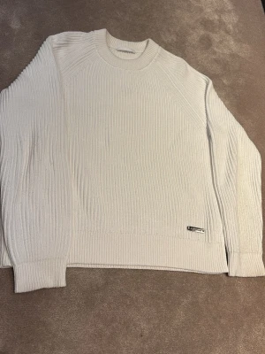 Vit ribbad stickad tröja Helmut Lang - Säljer en clean vit stickad tröja från Helmut Lang i storlek M. Tröjan har ribbad struktur, rund halsringning och en liten metallbricka vid nederkanten. Perfekt till lager på lager under höst och vinter.
